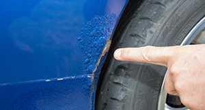 a person pointing at rusting paint on a wheel arch