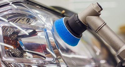 an auto mechanic using a small buffer to clean and polish the headlights of a car
